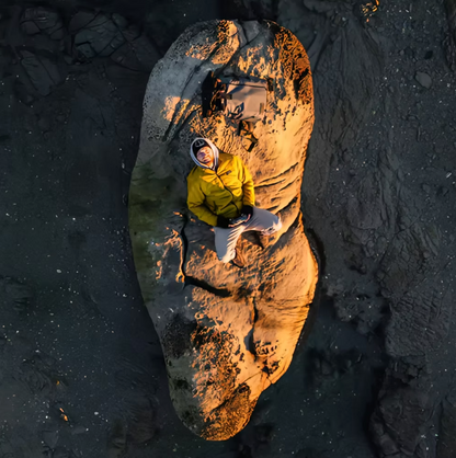 Person in yellow jacket sitting on a large rock with a backpack