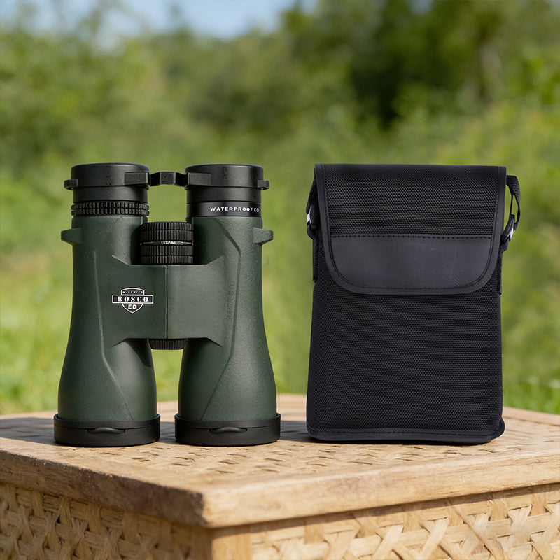 Green Bosco Apex HD-X1 Binoculars with a black carrying case on a wooden surface outdoors.