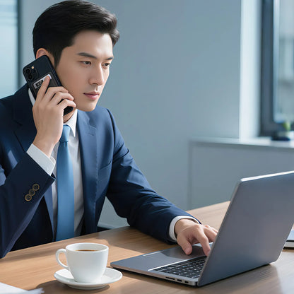 Man in a suit using a laptop and talking on a phone at a desk with a cup of coffee.