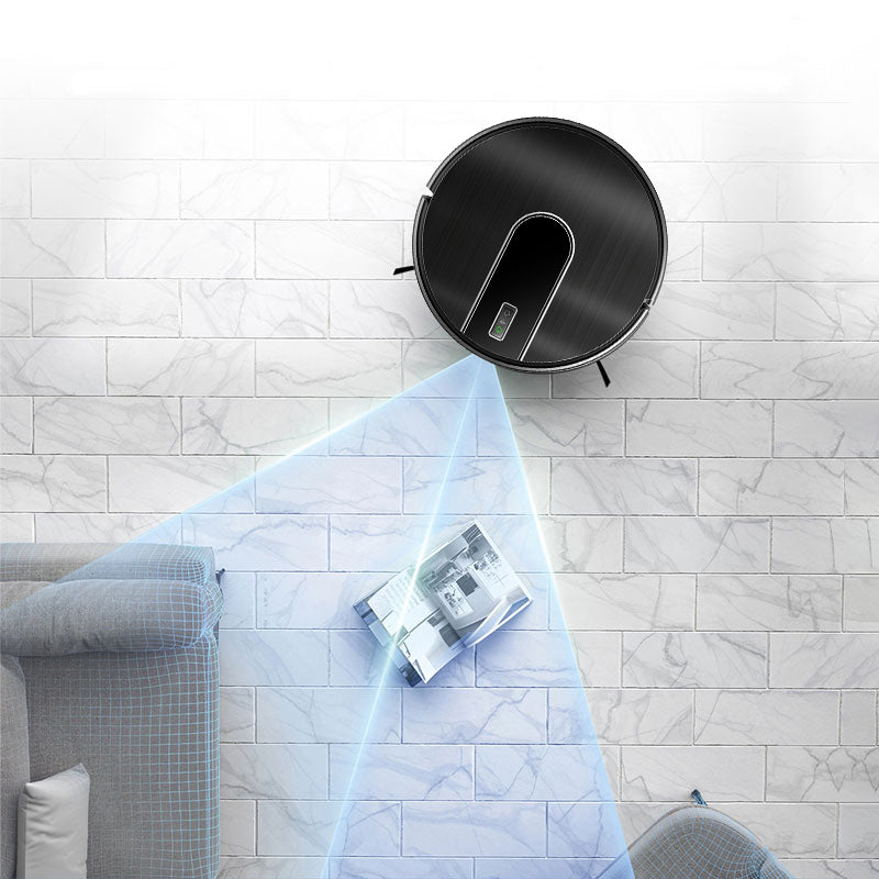 A round black Bytech Robot Vacuum Cleaner mounted on a white marble-look tiled wall, with a blue light beam projecting downward onto a magazine on the floor. Part of a gray sofa and chair are visible in the room setting.