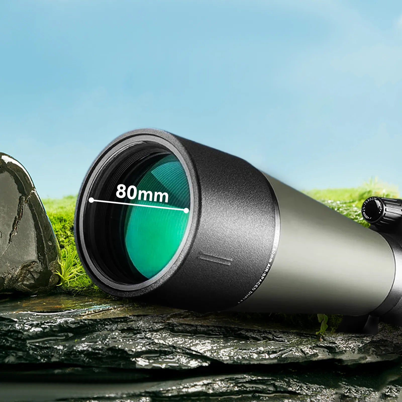 A close-up of a Noxus Spotting Scope eyepiece and objective lens assembly resting on wet rocks with grass and blue sky in the background. White text overlaid on the lens reads '80mm'.